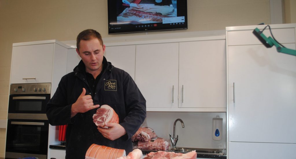 a man holding a piece of pork, talking about the different areas of the meat