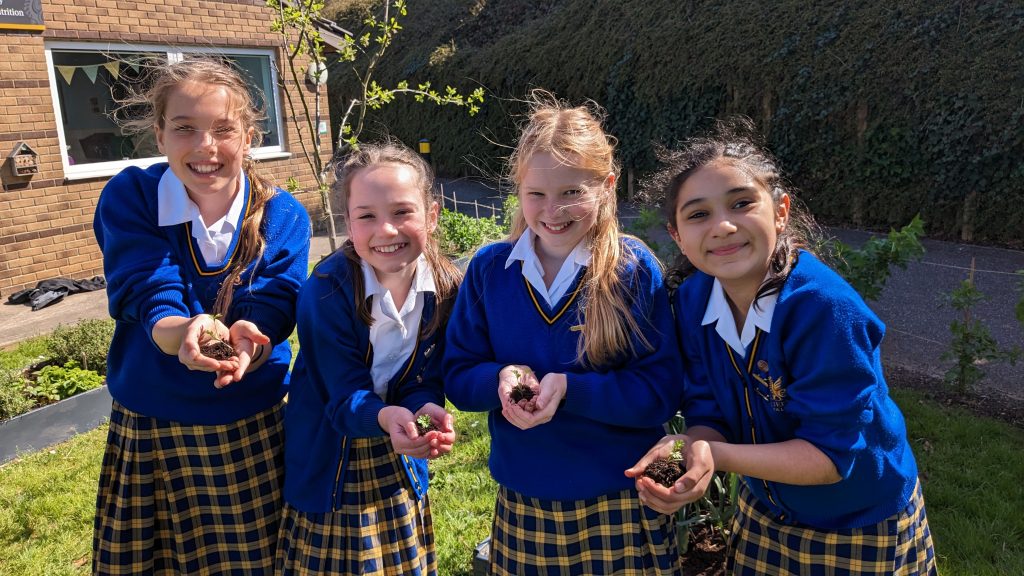 Queen's College students happily showing the seedlings they are about to plant in the ground