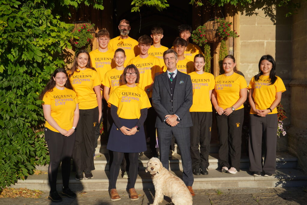 A group of pupils and staff standing on the steps of Queen's College wearing brightly coloured giving day tshirts