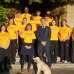 A group of pupils and staff standing on the steps of Queen's College wearing brightly coloured giving day tshirts