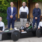 Queen's College Taunton Greenpower racing motorsports engineering team showing off their new kit sponsored by Brown & Brown, posing in the car, with Head of DT Mr Ben Higgs, and Brown & Brown.